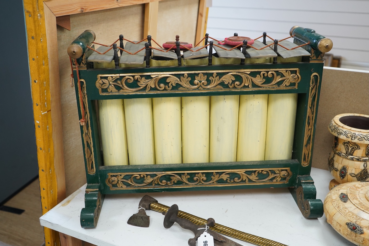 A green and gold painted wooden Javanese Gamelan Slenthem musical instrument, 61cm wide, 46cm high, together with two hammers